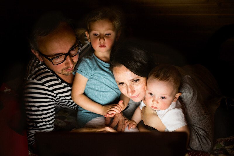 Young parents with little children and laptop at night.