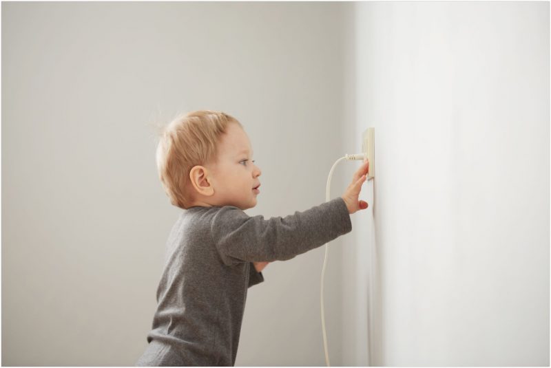 Curious little boy playing with electric plug. Trying to insert it into the electric socket.